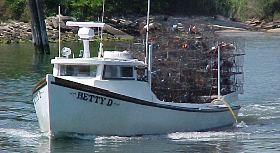 A crabbing vessel motoring along in the water with crab pots stacked in its hold with text: Betty D.