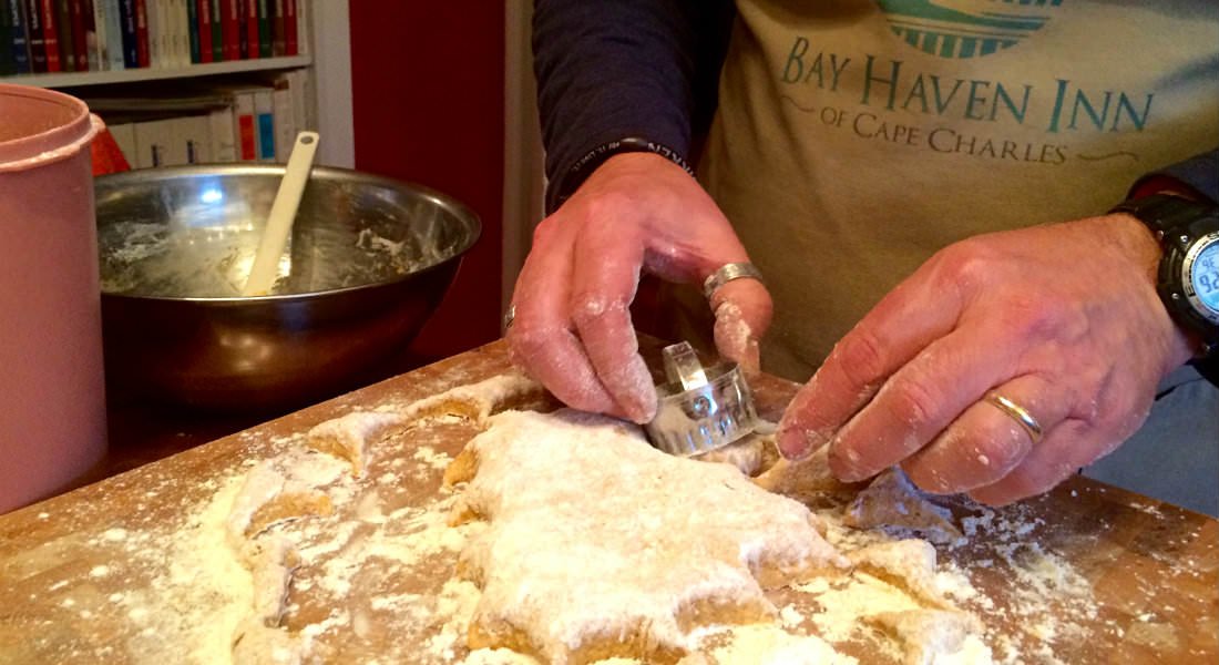 A man wearing a beige apron uses a cutter to section off pieces of floured dough.