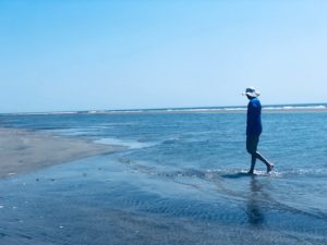 A man with a beige sun hat and blue shirt walks in the water on the Eastern Shore.