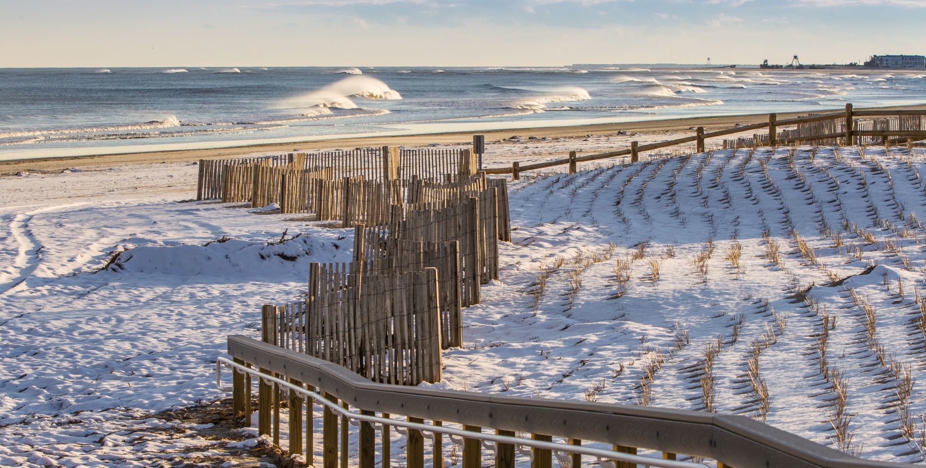Waves rolling in on the beach with the sand covered in snow and lined with snow fences