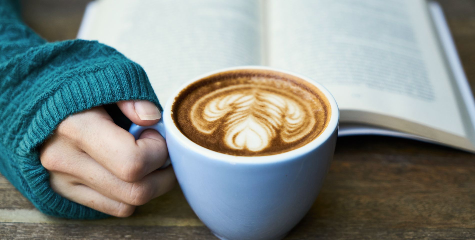 A person reading a book and drinking a latte at a coffee house