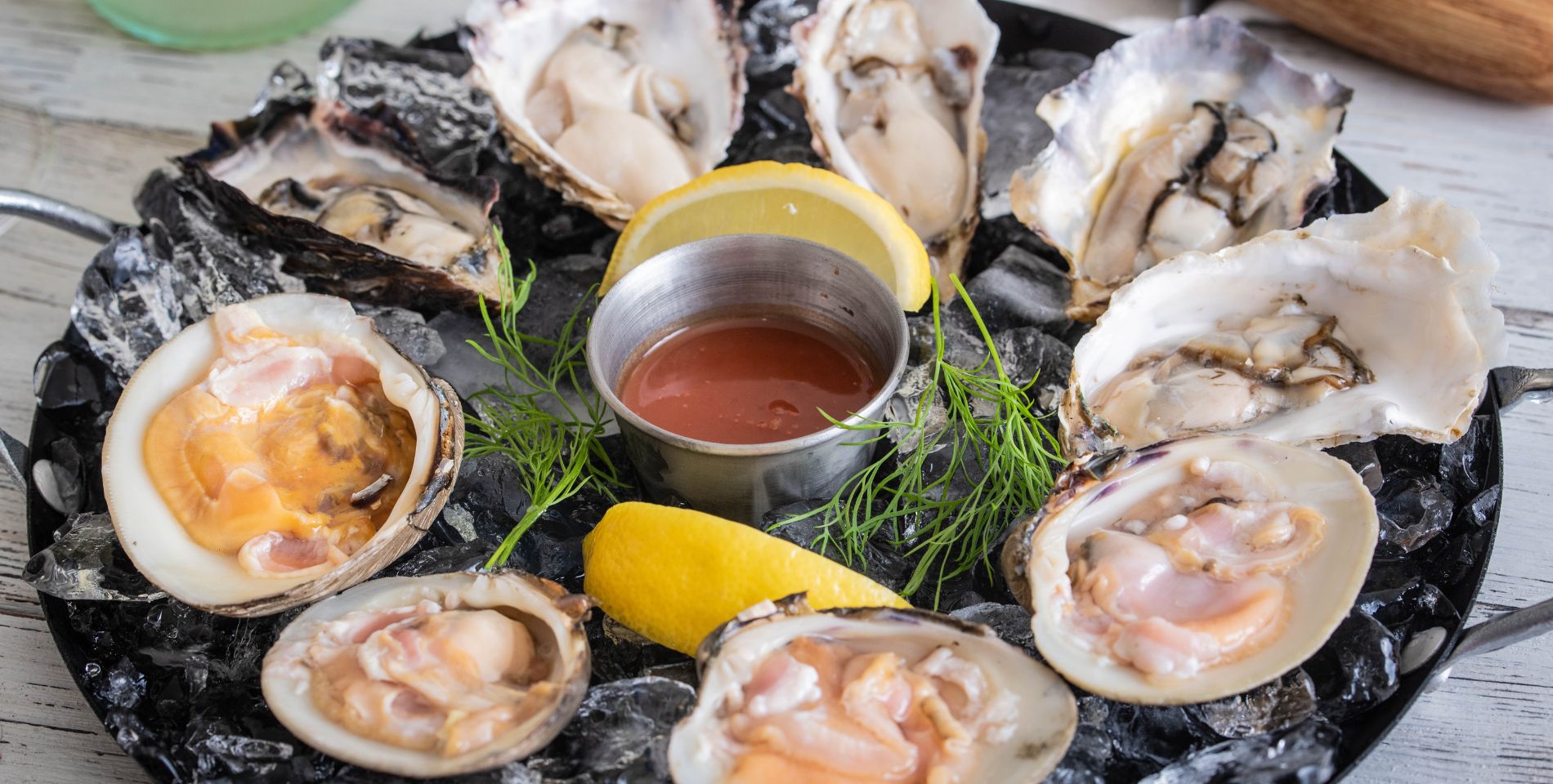 raw oysters and clams on a platter with fresh lemon wedges and sauce