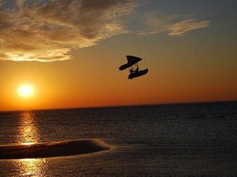 A silhouetted windsurfer catches air above the Bay with a golden sunset in the background. 