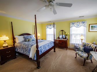 A four post bed with blue and white patterned comforter and pillows with yellow walls and beige carpet. 