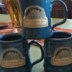 A stack of three blue coffee mugs with beige logos and the text: Bay Haven Inn of Cape Charles.