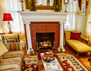 A couch and a chair near a red brick fireplace with a white posted mantle. 
