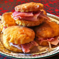 Sweet potato biscuits with Virginia ham on a floral print plate on a red tablecloth. 
