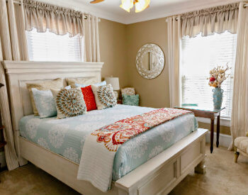 A bed with a light green and white comforter and white washed bedframe in the Georgie Wilson room. 