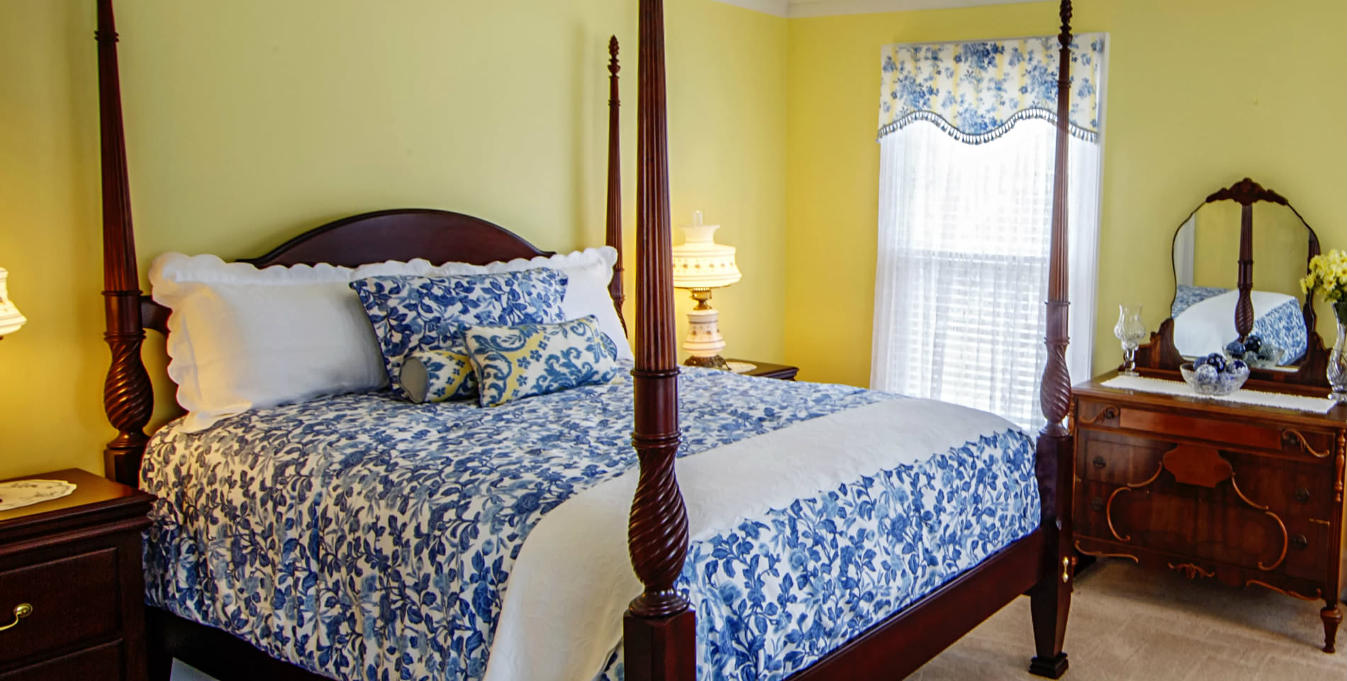The bed with a blue a white floral print comforter and throw pillows and plush white pillows by the headboard. 