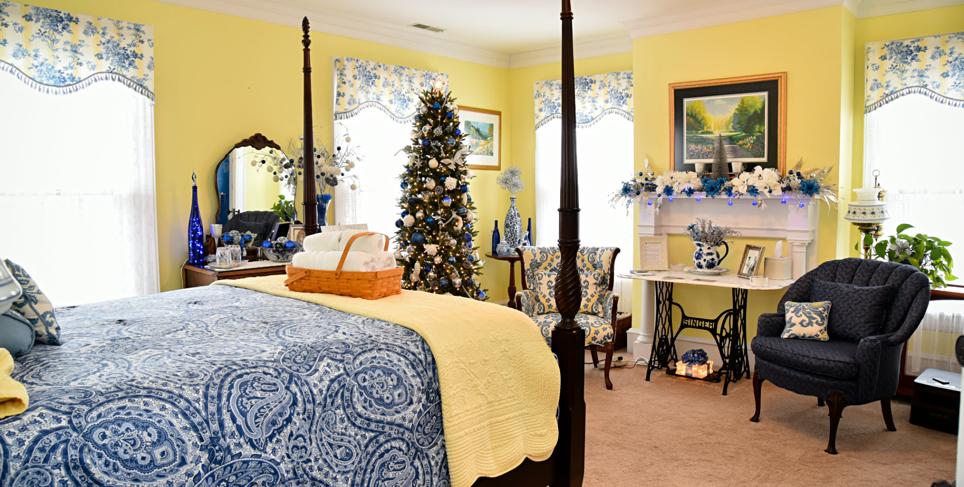 A basket of plush white towels in a wood basket on the foot of the bed, festive decorations in the room. 