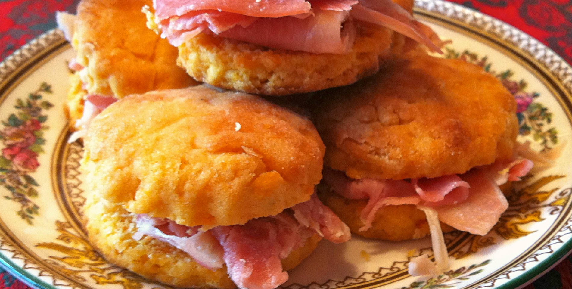 Sweet potato biscuits and Virginia ham served on a floral print plate atop a red tablecloth. 