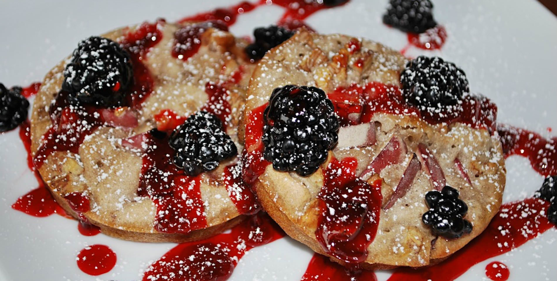Blackberries and a drizzle of red fruit sauce over biscuits served on a white plate. 