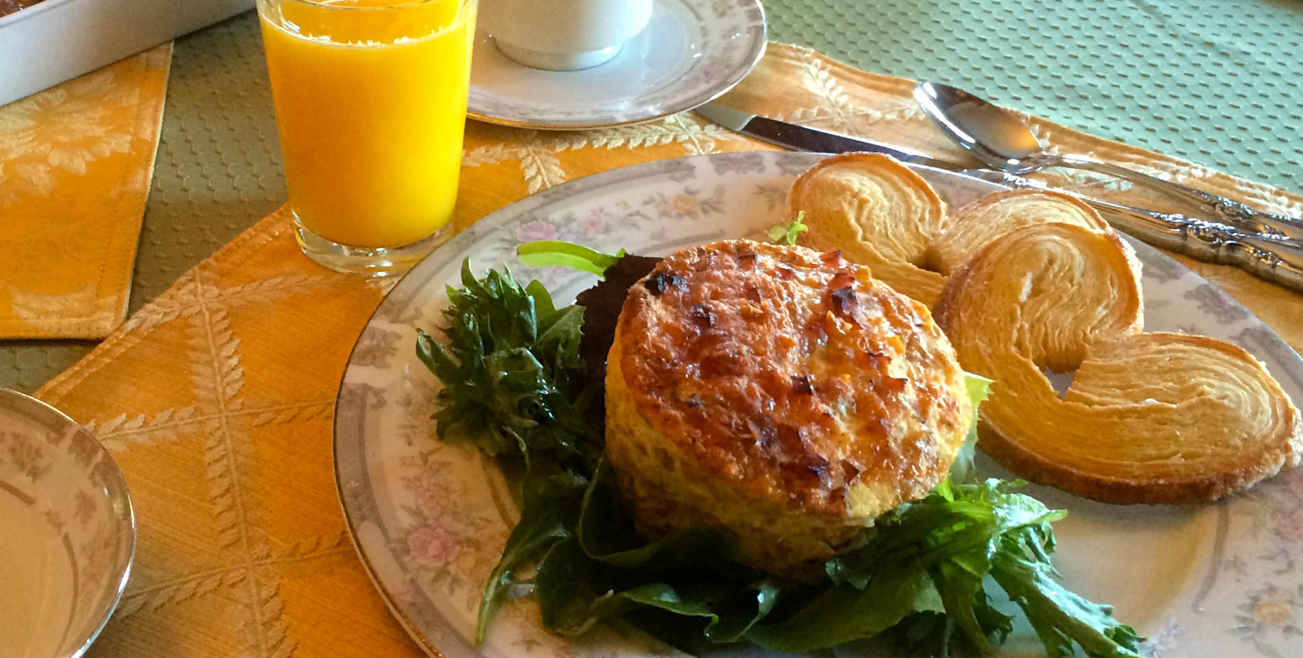 An omelette served with a bed of greens and two pastries with a glass of orange juice. 