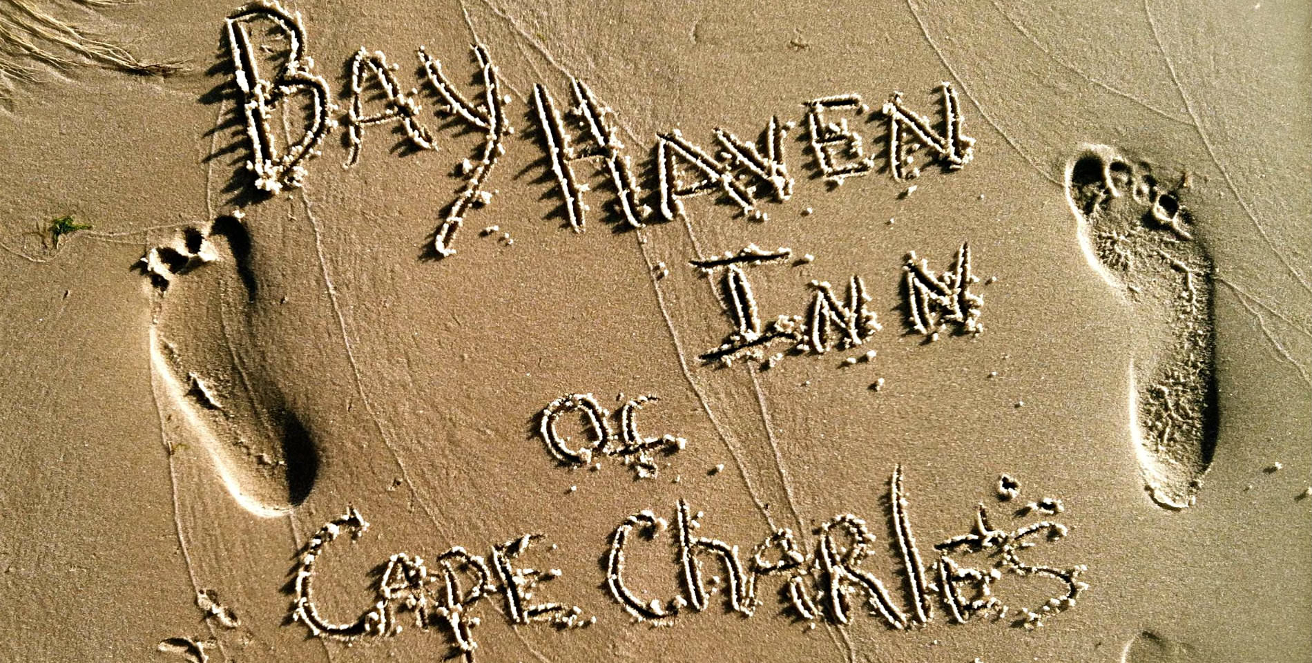 A golden sand beach with the finger written text: Bay Haven Inn of Cape Charles. 