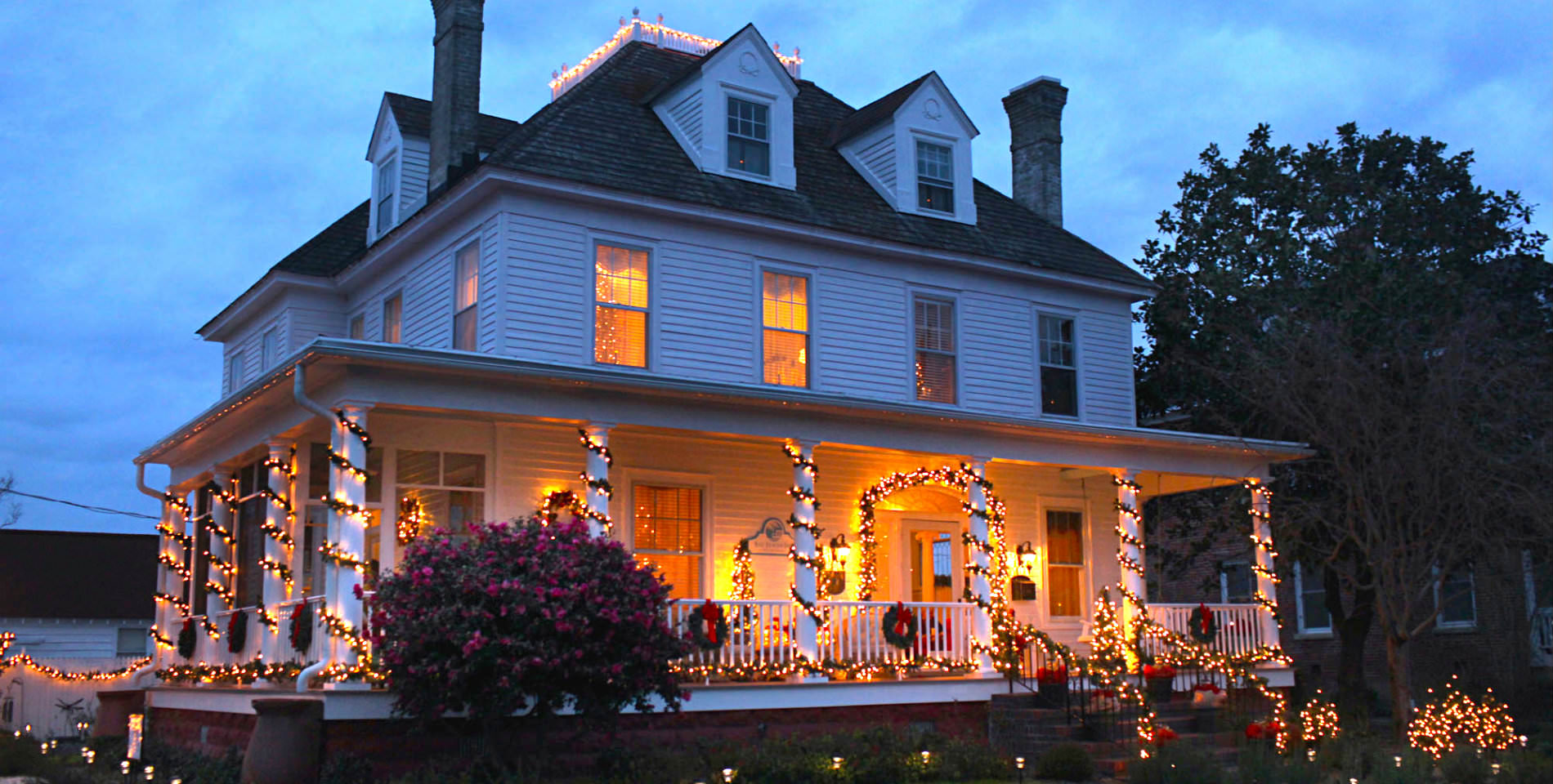 The post's of the Inn's front porch decorated with festive lights, the indoor lights glow warm from inside. 