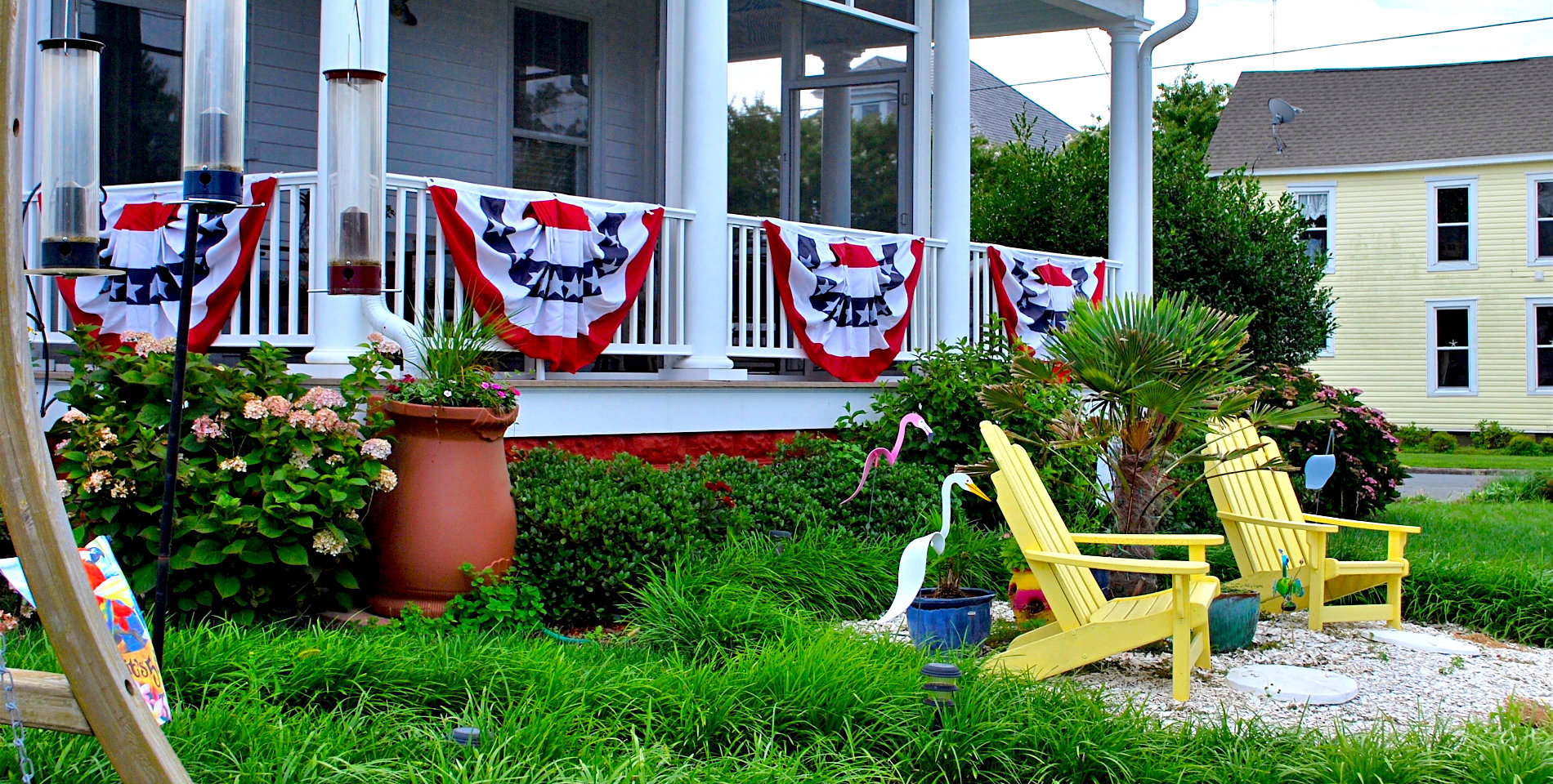 Two yellow Adirondack chairs before the front porch decorated with red, white and blue patriotic sashes. 