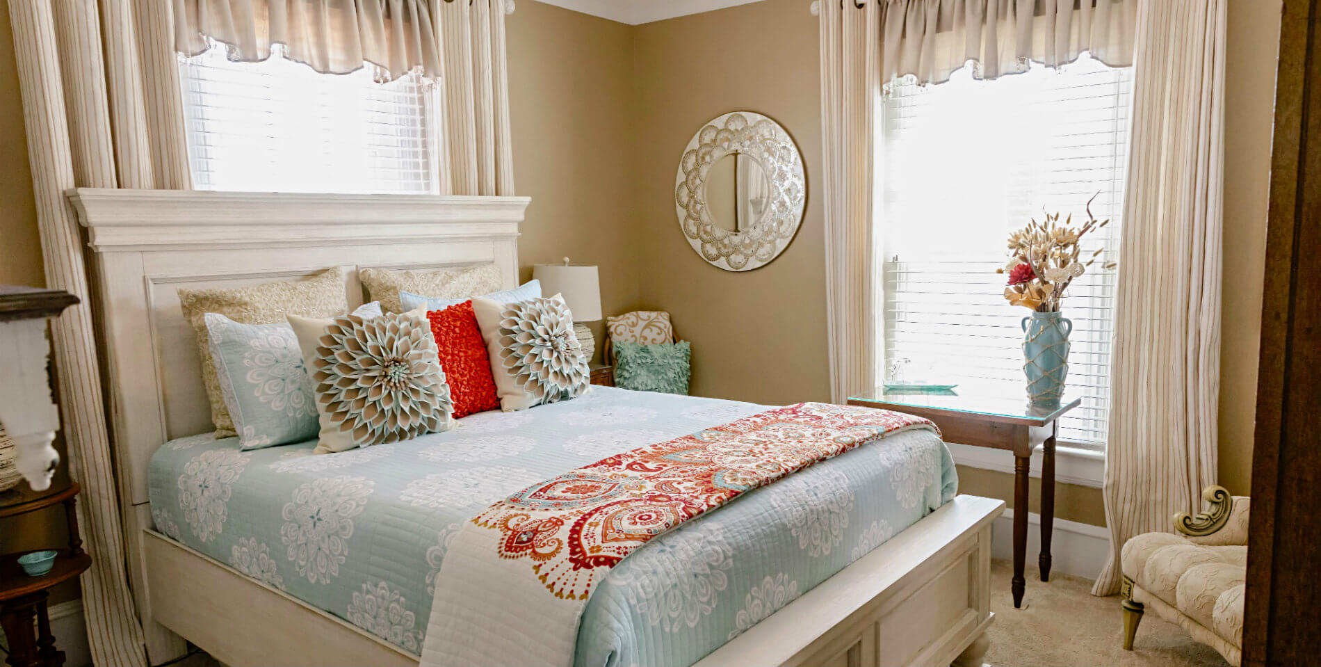 A bed on a white-washed wooden bedframe with many decorative throw pillows and beige walls. 