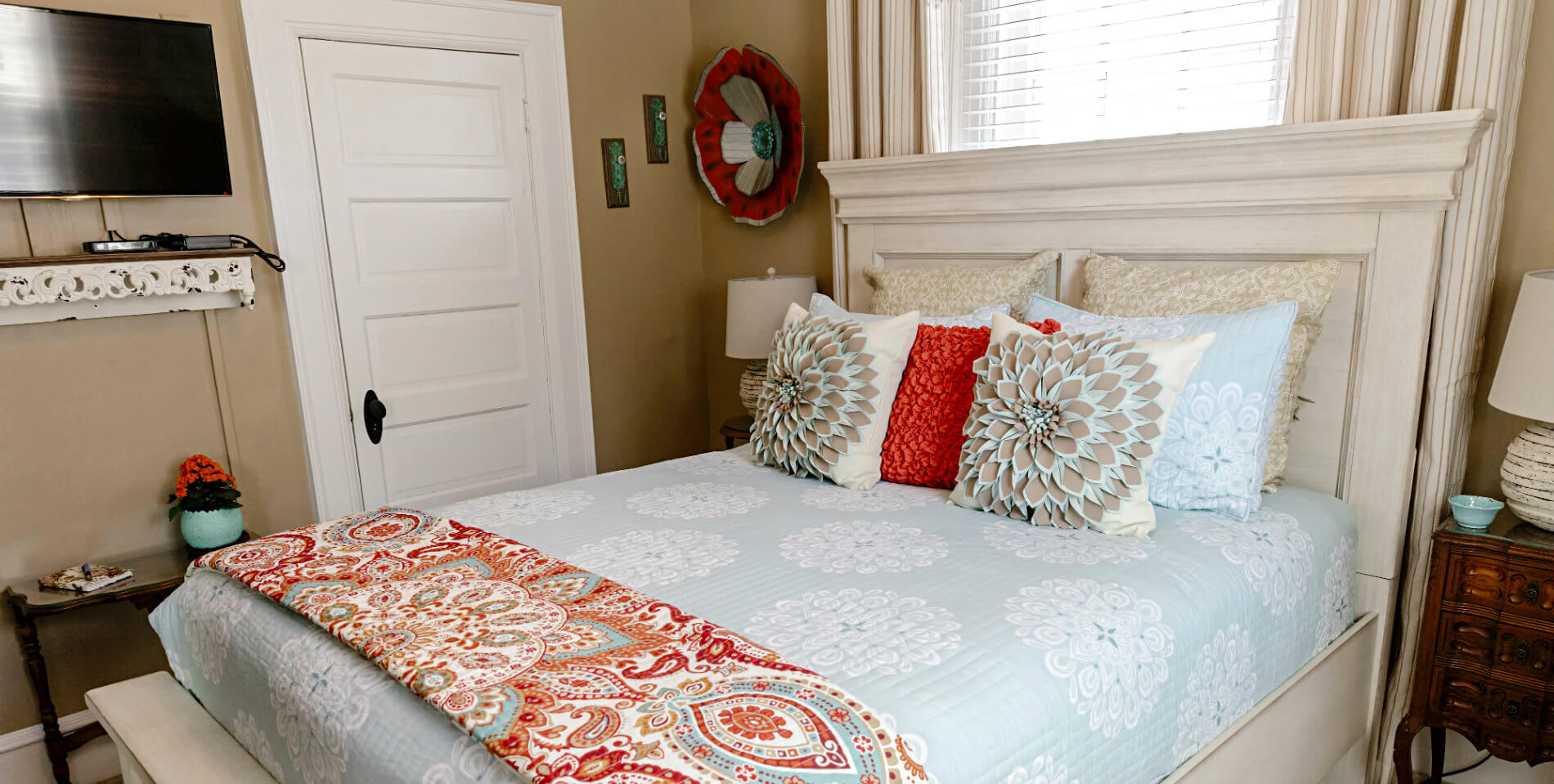 A bed on a white-washed wooden bedframe, a red paisley print throw at the foot of the bed. 