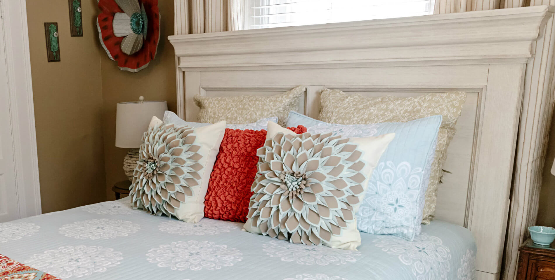 Red, beige, light blue and floral print throw pillows on the bed resting on the headboard. 