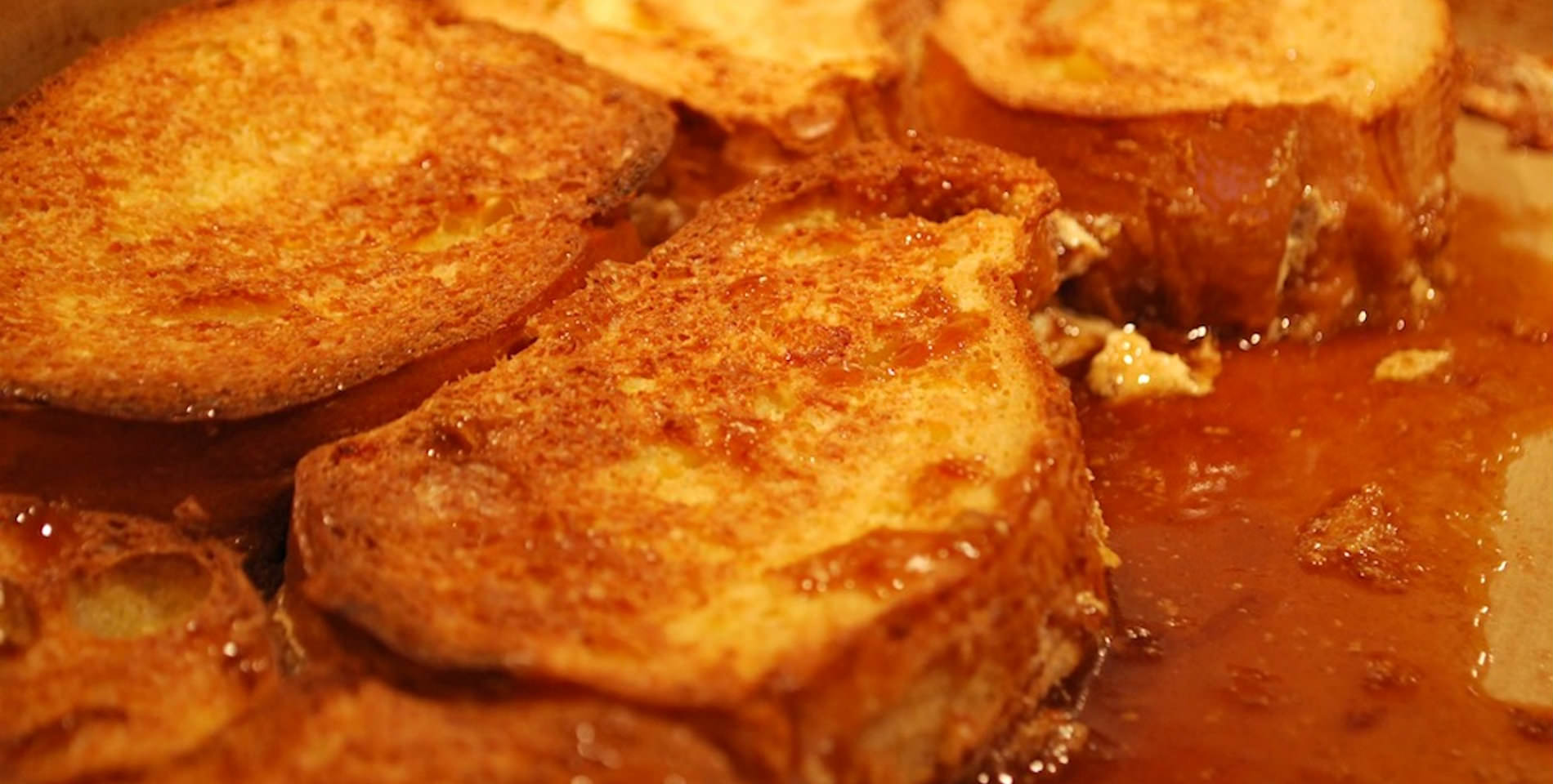 Fresh, golden brown French toast sits in a gooey drizzle of warm syrup. 