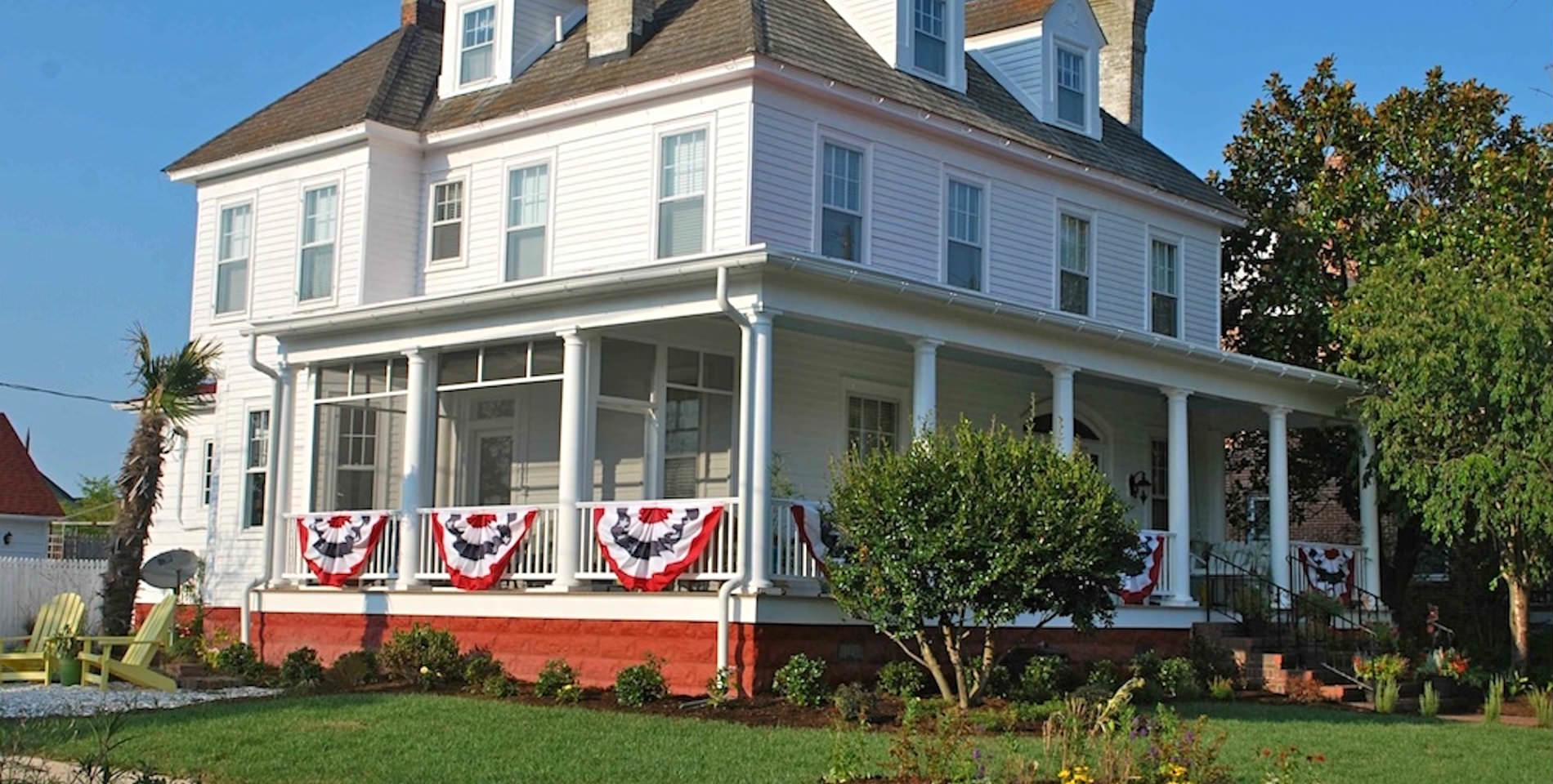 The Inn with a large wraparound front porch with red, white and blue festive bunting hanging from the porch railing. 