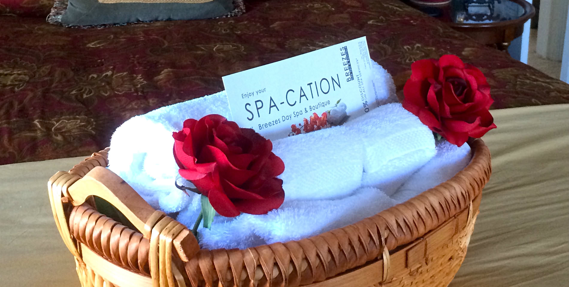 A bundle of plush white towels in a wicker basket with two red roses and a card with text: Enjoy your SPA-CATION.