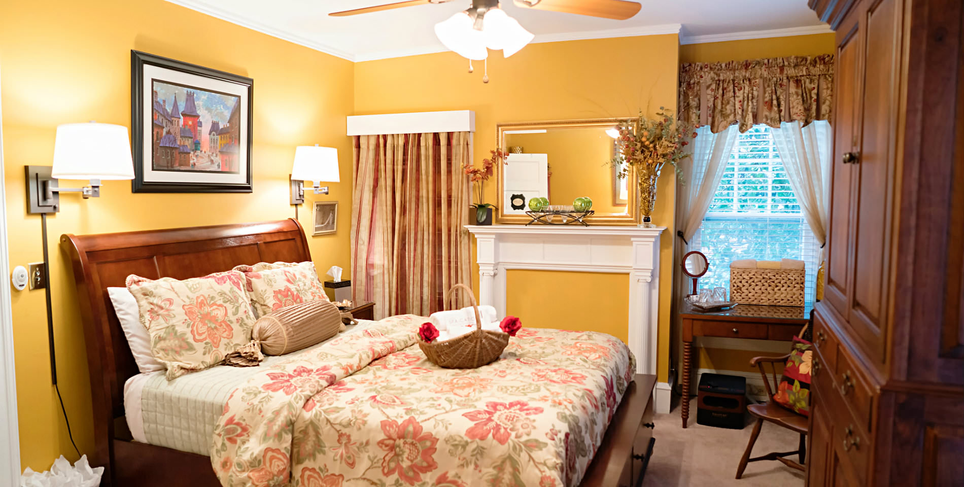 The bed with a basket of plush white towels atop the beige and floral print comforter near deocrative pillows. 