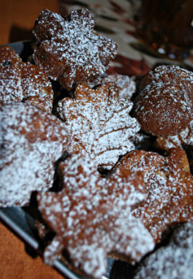 A half dozen brown, leaf-shaped pastries sit in a black tray covered in white powdered sugar. 