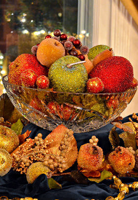 A glass bowl filled with decorative red, green, orange and purple fruit. 