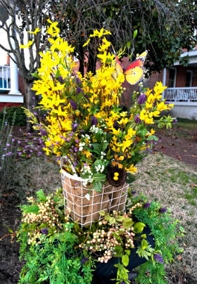 A white wire basket hold a bouquet of yellow, purple and white flowers. 