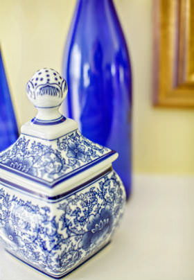 A white and blue patterned jar stands before two blue glass bottle on a white table. 