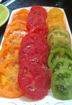 A large white serving platter with sliced orange, red and green tomatoes sprinkled with pepper. 