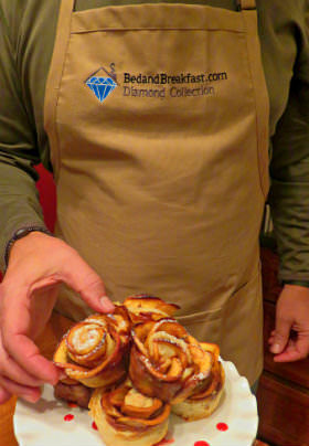 A man holding pastries wearing a beige apron with text: BedandBreakfast.com, Diamond Collection. 