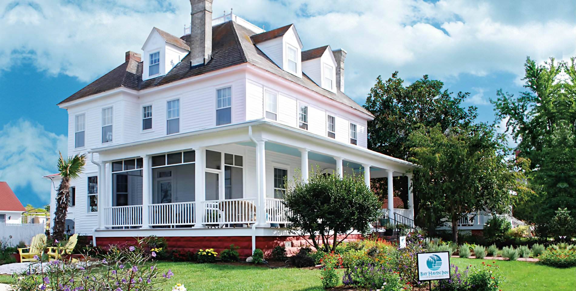 The stately Colonial-Revival style Inn with white siding and wraparound front porch. 